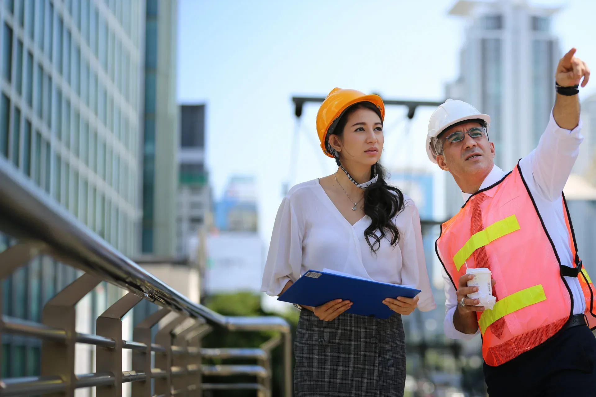 Engineers in hard hats collaborating on an elevated walkway against a city skyline
